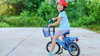 Happy child girl cycling in the park in the village for evening with sunset light exercise. Active child wearing bike helmet. Safety sports leisure with kids concept.